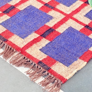 May include: A woven rug with a geometric pattern in shades of blue, red, and beige. The rug has a fringe border.