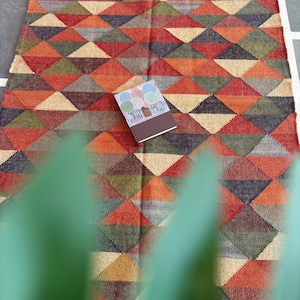 May include: A colourful rug with a geometric pattern of triangles in shades of red, orange, green, brown, and beige. The rug has a fringed border and is made of a woven material.