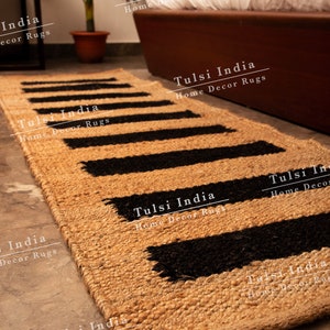 May include: A natural fibre rug with black and tan stripes. The rug is made of jute and has a woven texture. The rug is called "Tulsi India Home Decor Rugs".