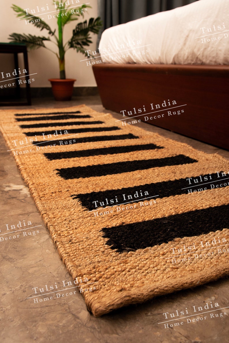 May include: A natural fibre rug with black and tan stripes. The rug is made of jute and has a woven texture. The rug is called "Tulsi India Home Decor Rugs".