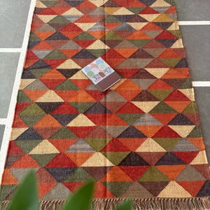 May include: A multicoloured geometric patterned rug with fringe on all sides. The rug is made of wool and has a variety of colours, including red, orange, yellow, green, blue, and brown.