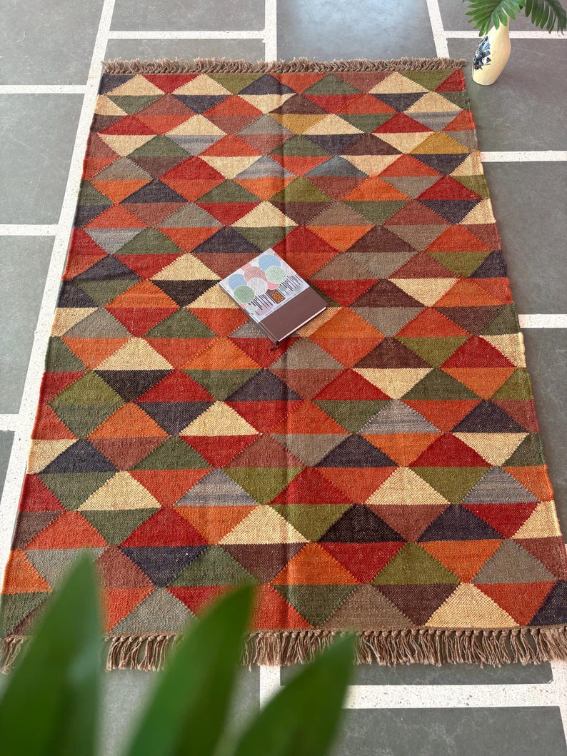 May include: A multicoloured geometric patterned rug with fringe on all sides. The rug is made of wool and has a variety of colours, including red, orange, yellow, green, blue, and brown.