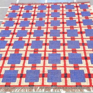 May include: A blue and red geometric patterned rug with a fringe border. The rug has a checkered pattern with squares of blue and red.