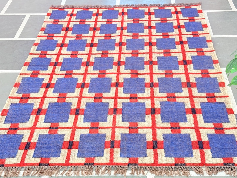 May include: A blue and red geometric patterned rug with a fringe border. The rug has a checkered pattern with squares of blue and red.