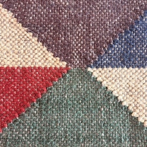 May include: Close-up of a woven rug with a geometric pattern in shades of brown, beige, red, green, and blue.