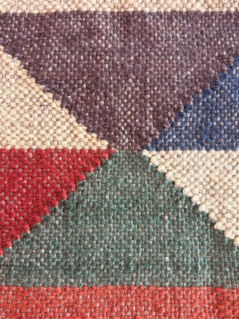 May include: Close-up of a woven rug with a geometric pattern in shades of brown, beige, red, green, and blue.
