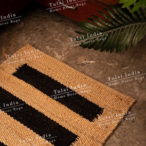 May include: A natural fibre rug with black stripes. The rug is made of jute and has a natural, earthy look. The rug is perfect for adding a touch of rustic charm to any room. The rug is made in India and is available in a variety of sizes.