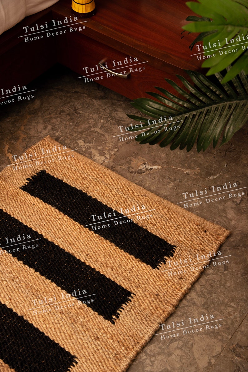 May include: A natural fibre rug with black stripes. The rug is made of jute and has a natural, earthy look. The rug is perfect for adding a touch of rustic charm to any room. The rug is made in India and is available in a variety of sizes.
