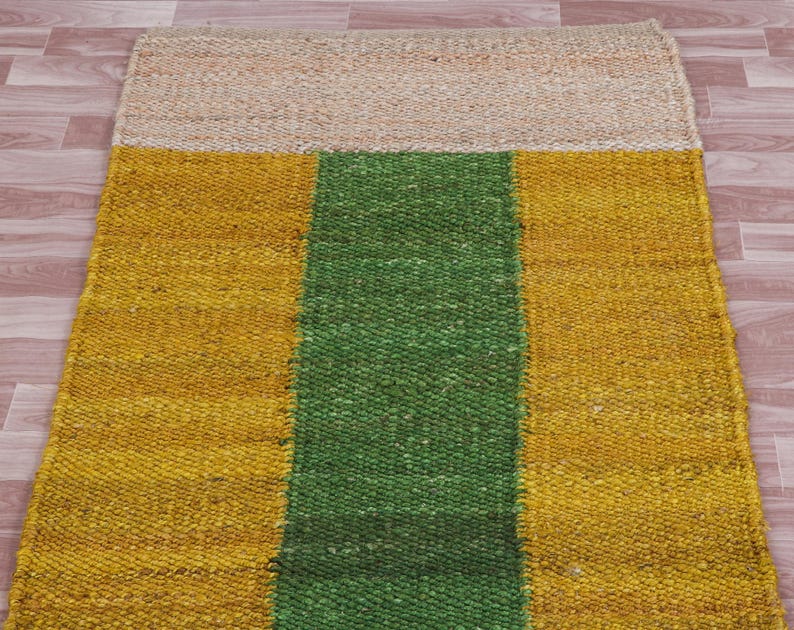 Pode incluir: Um tapete retangular de juta com uma faixa verde no centro e faixas amarelas de cada lado. O tapete tem uma textura natural e tecida.
