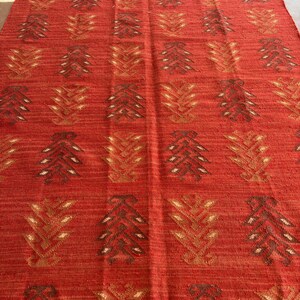 May include: Red area rug with a geometric pattern of brown and gold stylized leaves. The rug has a fringe border.