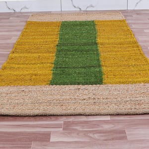 Pode incluir: Um tapete retangular de juta com um padr&atilde;o listrado em amarelo e verde. O tapete tem uma borda de juta natural.