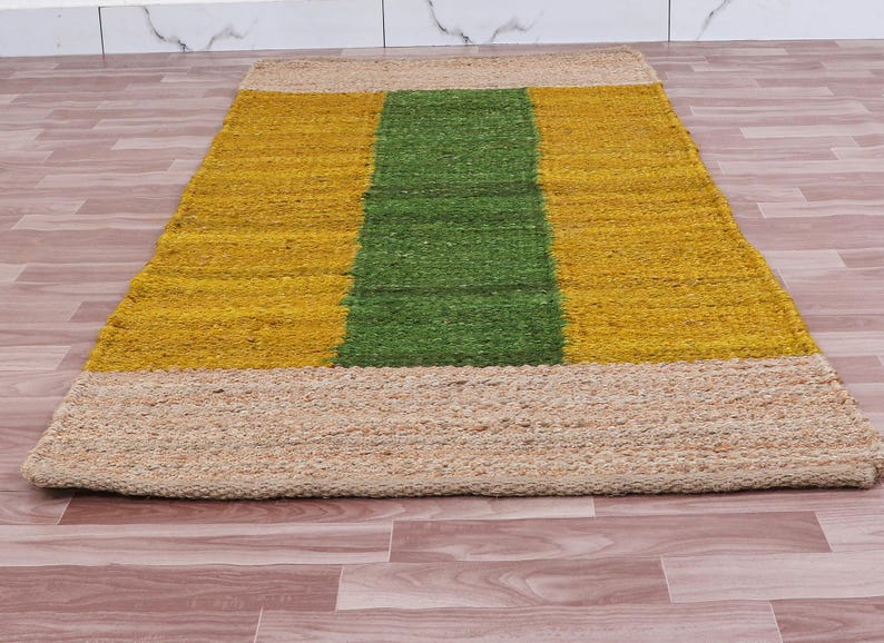 Pode incluir: Um tapete retangular de juta com um padr&atilde;o listrado em amarelo e verde. O tapete tem uma borda de juta natural.