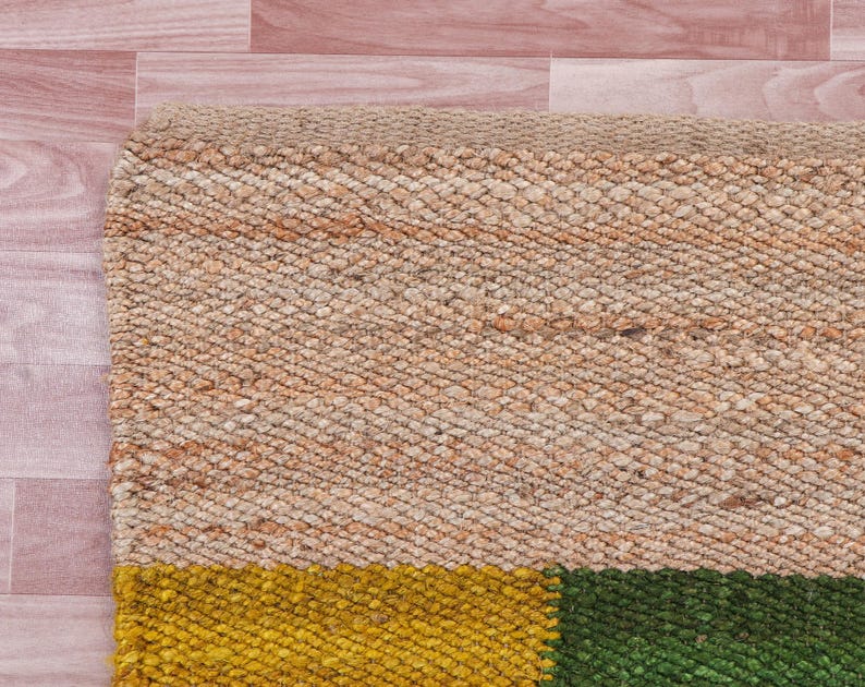 Pode incluir: Um tapete tecido com uma se&ccedil;&atilde;o superior bege natural e uma se&ccedil;&atilde;o inferior com tr&ecirc;s listras horizontais em amarelo, verde e marrom.