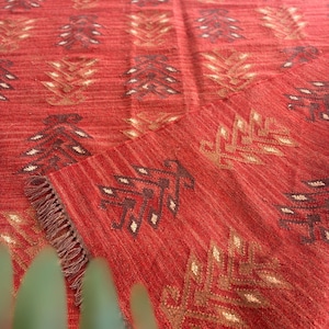 May include: Red area rug with a geometric pattern of brown and gold leaves. The rug has a fringe border.