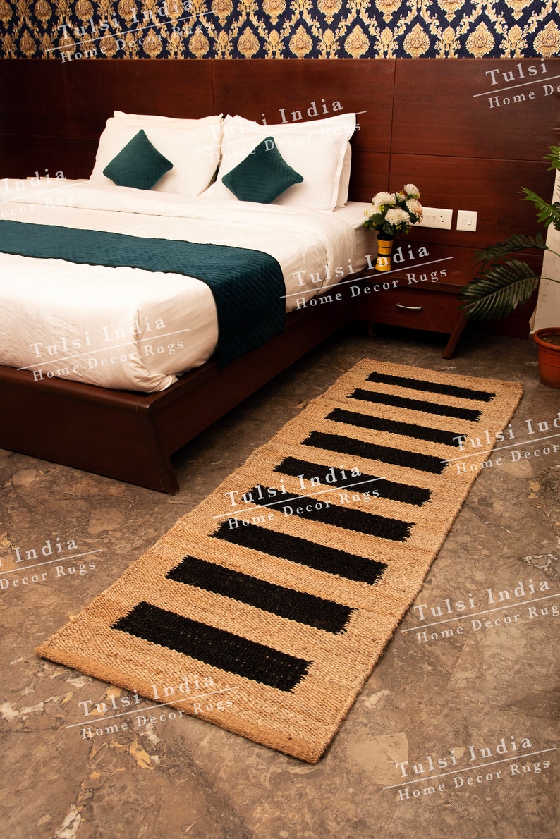 May include: A natural fibre rug with black stripes. The rug is made of jute and is perfect for adding a touch of natural beauty to any room. The rug is shown in a bedroom setting, placed in front of a bed with white bedding and teal throw pillows.