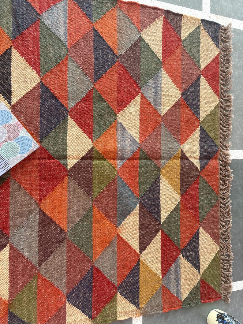 May include: A geometric patterned rug with a fringe border. The rug is made of woven jute and features a variety of colours, including red, orange, brown, green, and beige.