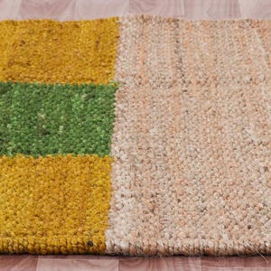 Pode incluir: Um tapete retangular de juta com um padr&atilde;o listrado em amarelo, verde e juta natural. O tapete &eacute; tecido com uma fibra natural texturizada.