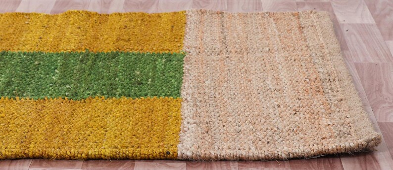 Pode incluir: Um tapete retangular de juta com um padr&atilde;o listrado em amarelo, verde e juta natural. O tapete &eacute; tecido com uma fibra natural texturizada.