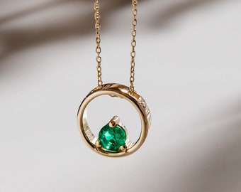 May include: A gold chain necklace with a circular pendant featuring a green emerald gemstone.