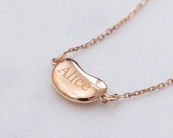 May include: A rose gold necklace with a bean-shaped pendant engraved with the name "Alice".