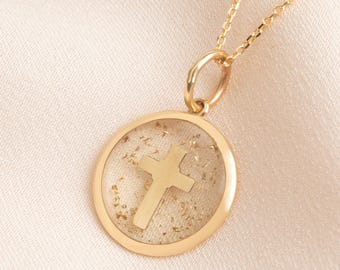 May include: A gold-colored necklace featuring a circular pendant with a cross design. The pendant has a clear center with gold flecks and a gold-colored cross. The necklace chain is also gold-colored.