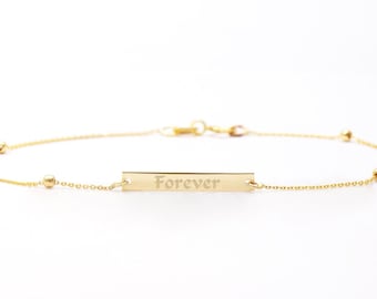May include: A gold chain bracelet with a small rectangular tag that says "Forever" and four small gold beads.