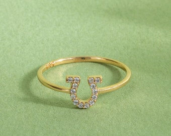 May include: A gold ring with a horseshoe design set with clear cubic zirconia stones.