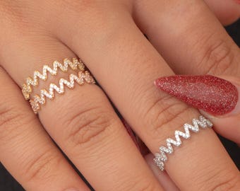 May include: Two rings with a zigzag design are displayed on a hand. One ring is gold-toned, and the other is silver-toned. Both rings are adorned with small, sparkling stones. The hand has red glitter nail polish.