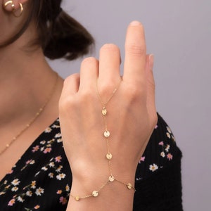 Könnte beinhalten: Ein goldenes Kettenarmband mit kleinen runden Anhängern. Das Armband ist so konzipiert, dass es am Handgelenk getragen wird und den Arm hinaufreicht, wobei die Kette bis zum Finger reicht.