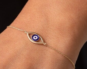 May include: A gold chain bracelet with a blue evil eye charm. The charm is a circle with a white center and a blue outer ring.