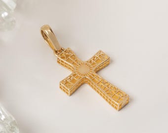 May include: A gold-toned cross pendant featuring an intricate, open-work lattice design throughout its structure. The center of the cross displays a smooth, circular medallion, and the piece includes a polished bail at the top for attachment.