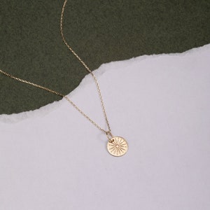 Pode incluir: Um colar de ouro com uma corrente delicada e um pingente redondo com um design de sol.