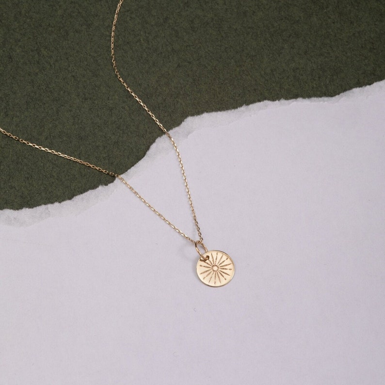 Pode incluir: Um colar de ouro com uma corrente delicada e um pingente redondo com um design de sol.
