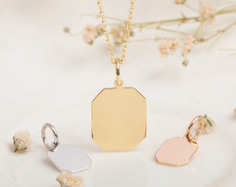 May include: A gold-colored necklace with a rectangular pendant is displayed. Two smaller pendants, one silver and one rose gold, are also shown. The pendants have an octagonal shape. The jewelry is presented on a white surface with small, dried flowers.