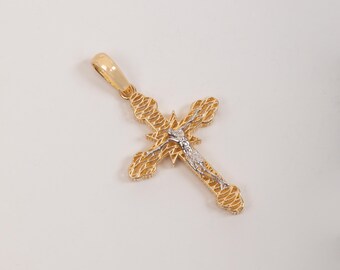 May include: A gold cross pendant featuring a textured, openwork design with a central star-shaped element. A silver-toned figure of Jesus is positioned on the front of the cross, which includes a polished gold bail at the top for attachment.