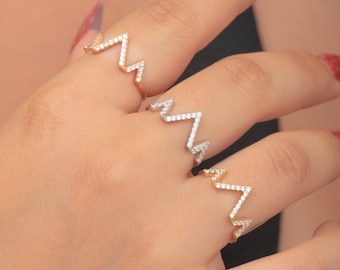 May include: Three gold and silver zigzag rings, each adorned with small, sparkling white gemstones. The rings are displayed on a hand, showcasing their delicate design and intricate details. The rings are a stylish accessory.