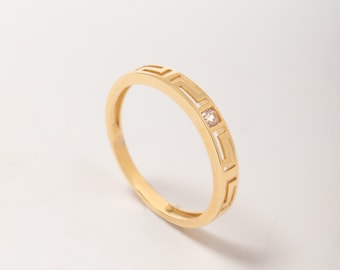 May include: A gold ring with a geometric design and a small, clear gemstone. The ring is set against a white background, highlighting its polished finish and intricate details. The ring's design features a series of rectangular cutouts.