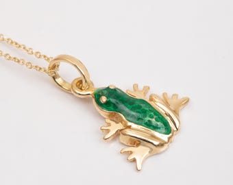 May include: Gold-toned necklace featuring a frog pendant. The pendant has a green enamel body and gold-colored details. The frog is in a crouching position, with its legs and eyes visible. The chain is also gold-toned.