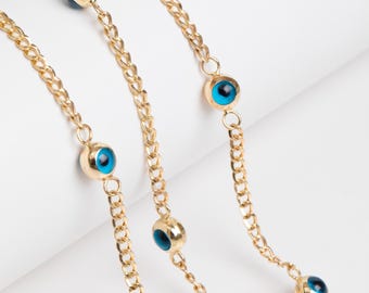 May include: Two gold chains with blue evil eye charms. The chains are layered on a white surface.
