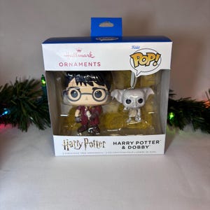 May include: A boxed set of two Harry Potter Christmas tree ornaments. One ornament is of Harry Potter in a maroon robe, and the other is of Dobby. The box reads "Hallmark Ornaments" and "Harry Potter & Dobby".