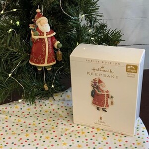 May include: A Hallmark Keepsake Series Edition ornament featuring Santa Claus with a sack of gifts and a lantern. The ornament is red and gold with a pull string movement. The box reads "Magic Pull String Movement".