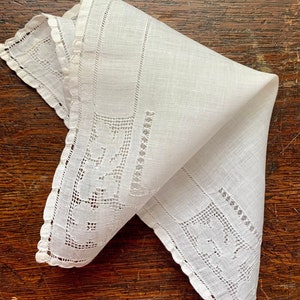 May include: A white linen handkerchief with delicate lace edging and a floral pattern. The handkerchief is folded in a triangle shape.
