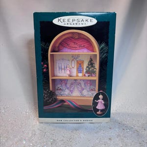 May include: Keepsake Ornament box featuring a miniature stage set from "The Nutcracker Ballet." The box is dark green with a decorative ribbon. Inside, a miniature stage with a ballerina, Christmas tree, and stage curtains.