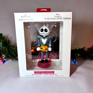 May include: A Hallmark Christmas tree ornament featuring Jack Skellington from Tim Burton's "The Nightmare Before Christmas." The nutcracker figure is in a clear plastic case. Jack is in a black and white pinstripe suit, holding an orange pumpkin. The box reads "Hallmark Ornaments."