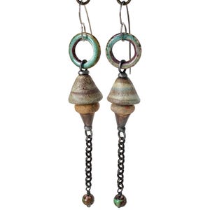 May include: A pair of handcrafted dangle earrings. Each earring features a teal ceramic ring, a stacked cone-shaped ceramic pendant, and a chain ending in a small bead. The earrings are suspended from silver-tone ear wires.