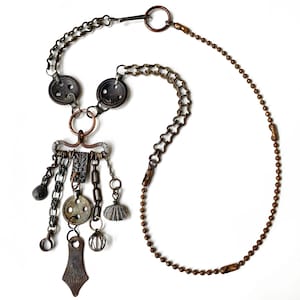 May include: A handcrafted necklace featuring a variety of antique-style charms and chains in shades of bronze and silver. The necklace includes button accents, a decorative pendant, and a ball chain. The design is intricate and detailed, with a vintage aesthetic.