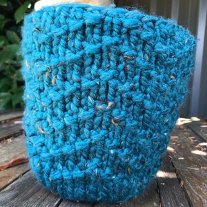 Pode incluir: Um chapéu de malha azul turquesa com um padrão de ponto texturizado. O chapéu é feito de um fio grosso com manchas de cor por toda parte.