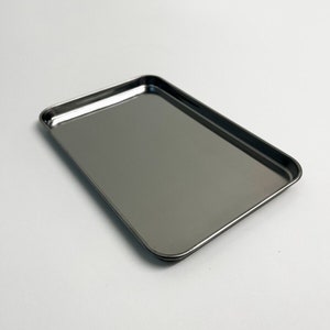 Puede incluir: Una bandeja rectangular de metal plateado con bordes ligeramente redondeados.