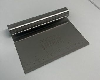 Peut inclure: Une spatule à pâtisserie en acier inoxydable avec une règle sur un côté. La règle est graduée en pouces et en centimètres. La spatule a une poignée roulée. Le texte sur la règle indique "Équivalents de mesure : CUP = 8 fl oz = 237 ml"