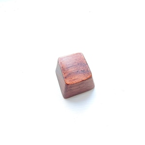 May include: A dark brown wooden keycap with a smooth, slightly textured surface.